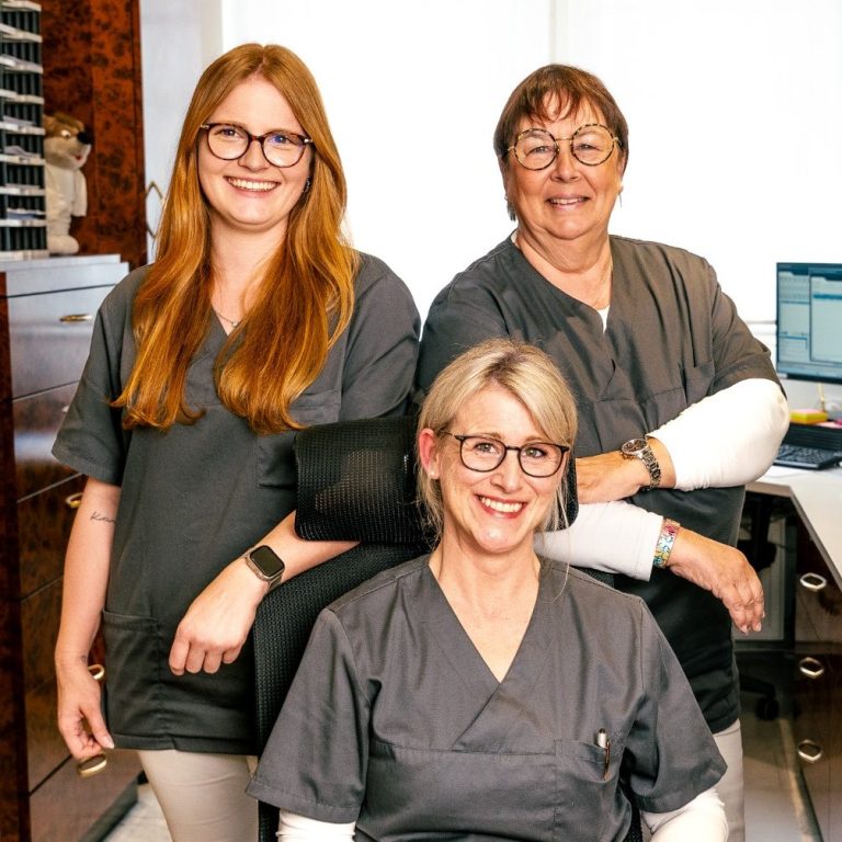 Anmeldung Team Drei Personen in Laborbekleidung lächeln, stehen und sitzen am Arbeitsplatz.