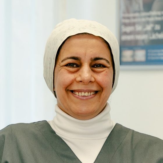 Dr. med. dent. Bothaina Alabdalla Frau mit Kopftuch und freundlichem Lächeln, trägt graue Arbeitskleidung.
